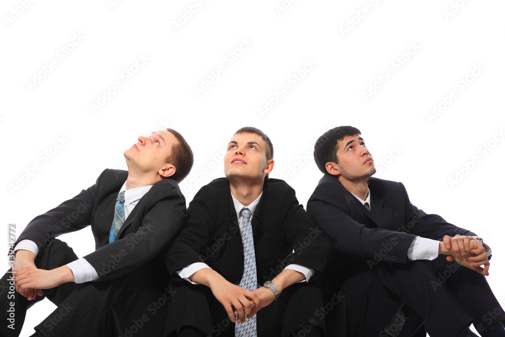 Three young businessmen sit on floor and look upwards