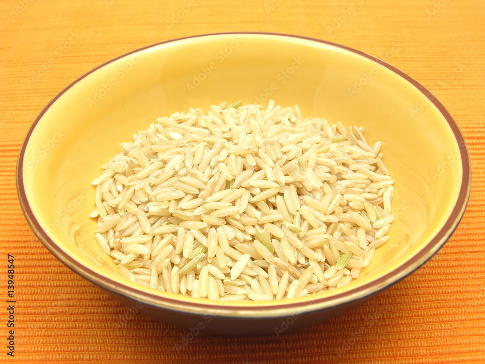 Keramikschale mit Naturreis vor orangem Hintergrund Keramikschale mit Naturreis vor orangem Hintergrund