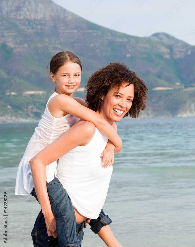 Mother giving daughter piggyback ride on the beach