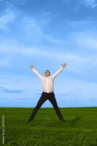 Businessman jumping on the green grass over clouds blue sky