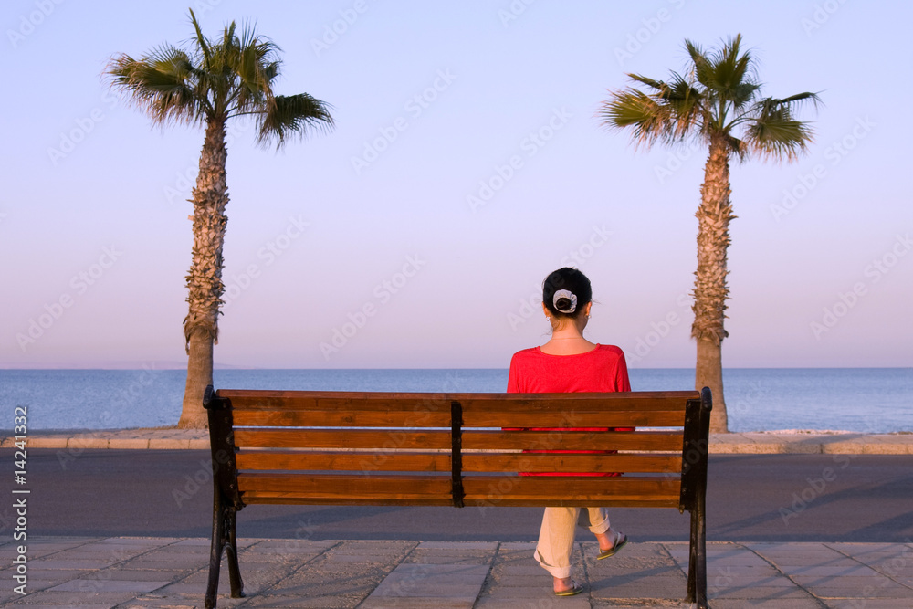 Lonely girl sits on a bench near sea beach
