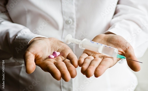 A doctor holding a handful of vitamin capsules and syringe