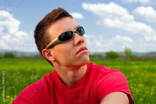 Teenager with sunglasses and red shirt looking up.
