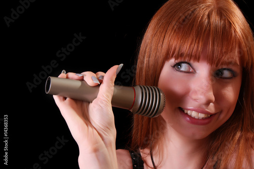 Young pretty woman singing with microphone on black background