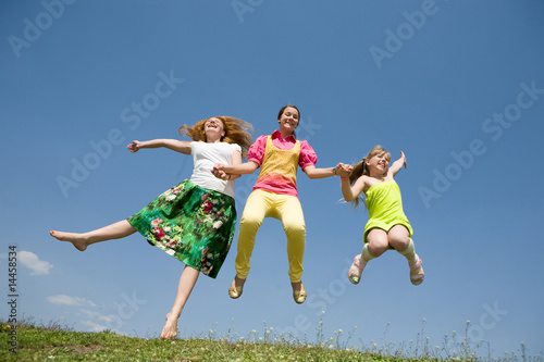 Happy Mom and two daughter jumping on green meadow