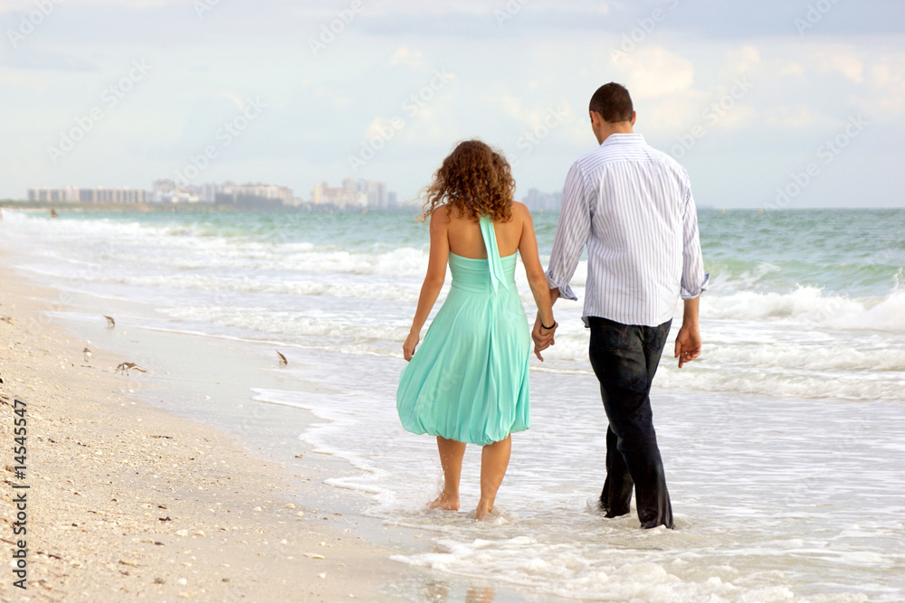 young couple walking hand in hand on the beach thier feet in the