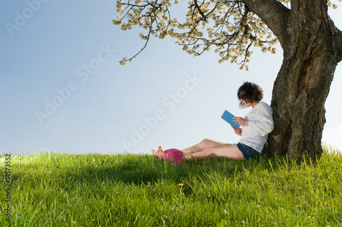 Young woman sitting under a blossom tree reads a book