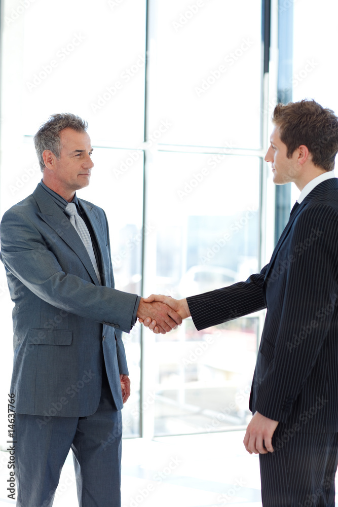 Senior and junior businessman shaking hands in agreement Senior and junior businessman shaking hands in agreement