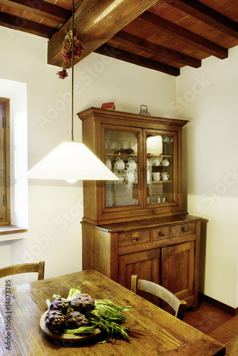 Interior of a rustic house in Tuscany Italy. Detail of the kitchen with sideboard and table, wooden ceiling and lamp photo