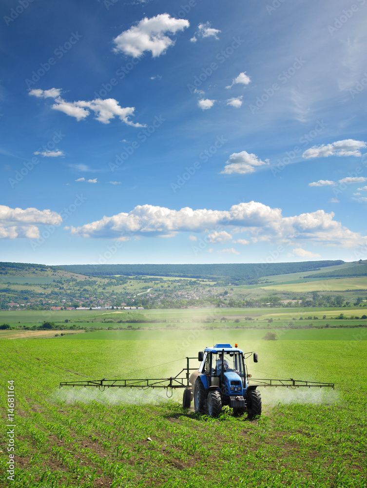 Fototapeta premium Farming tractor plowing and spraying on field vertical