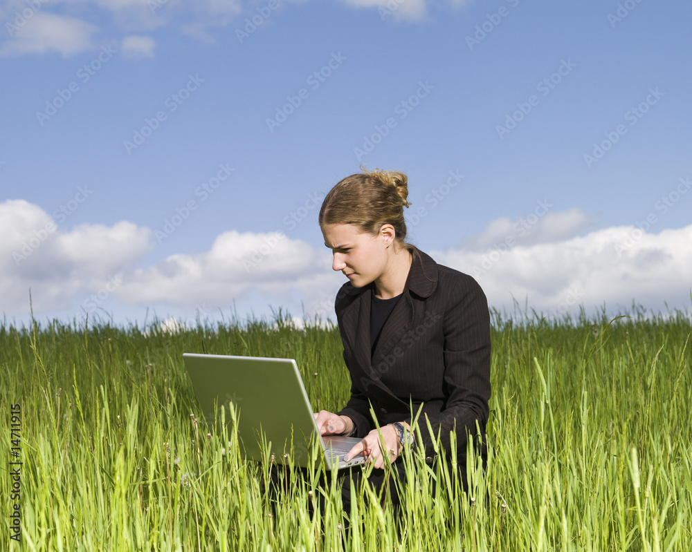 Woman sitting outdoor in thye grass with her laptop Woman sitting outdoor in thye grass with her laptop
