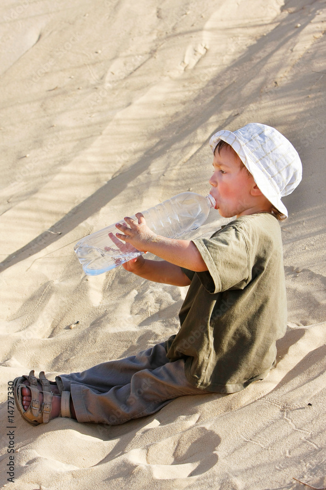 young boy drinking water in sand desert young boy drinking water in sand desert