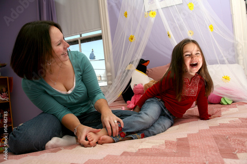mother tickling her little girl's bare feet on the bed