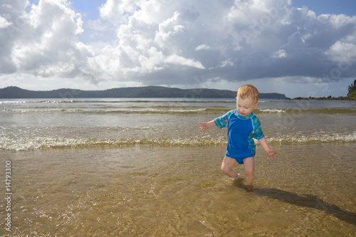 Toddler playing at beach in sunlight with impending storm photo
