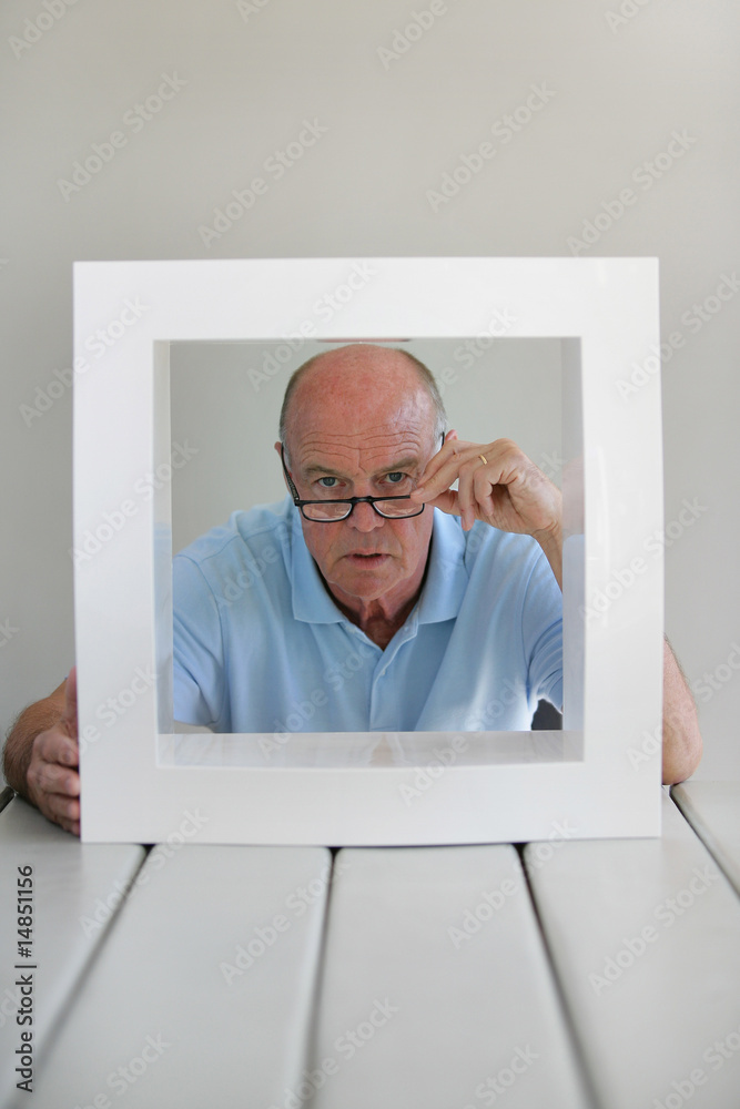 Fototapeta premium Portrait d'un homme senior derrière un cadre blanc