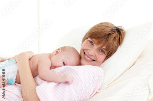 Mother with newborn baby in bed smiling at the camera