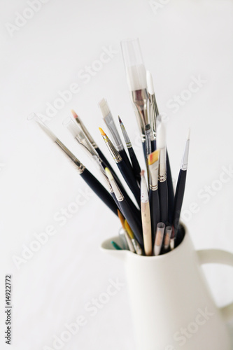 A set of paintbrushes in a white jug on a blank background.