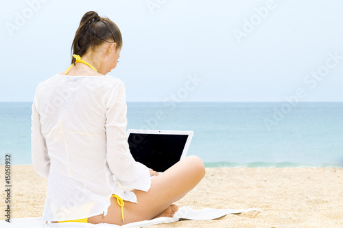Frau sitzt mit Laptop am Strand
