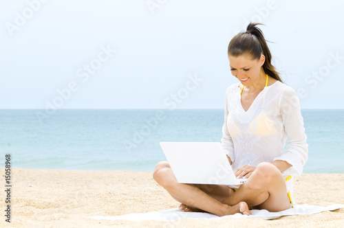 Hübsche Frau sitzt mit Laptop am Strand
