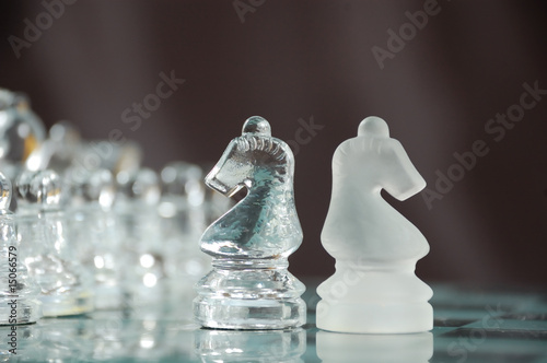 two glass knights on chessboard against black background