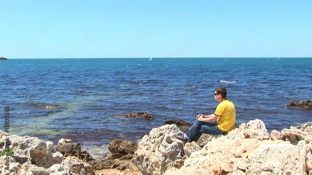 Young man in a yellow T-shirt sits on seacoast Young man in a yellow T-shirt sits on seacoast
