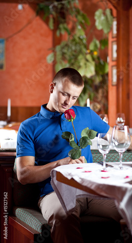 The man with a red rose sits at restaurant