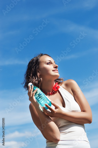 Smiling young woman holding bottle of water against blue sky