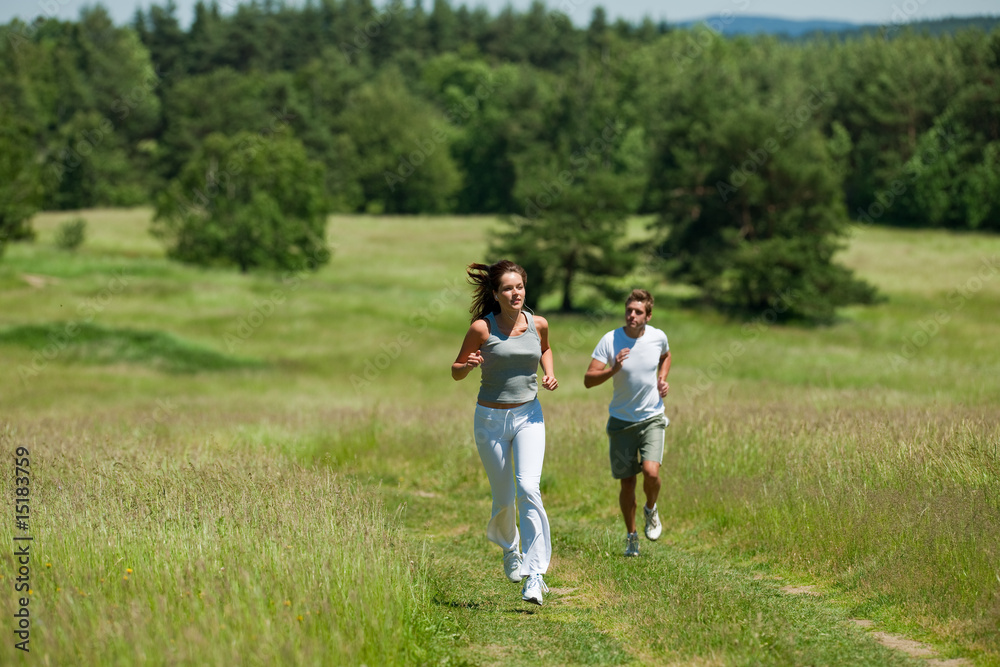Young woman with headphones jogging in a meadow