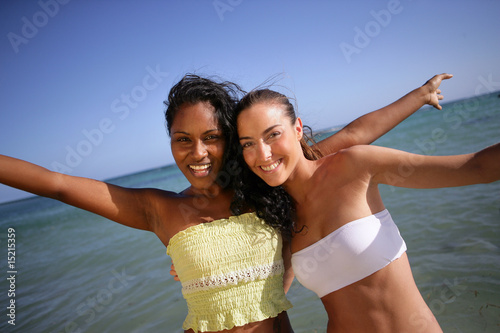 Jeunes femmes souriantes au bord de la plage levant les bras photo