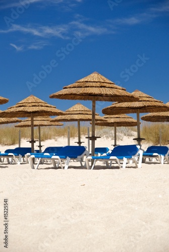 An area of straw sunshading umbrellas with beach chairs.