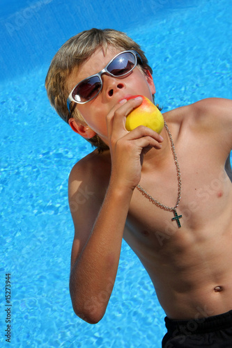 Junge mit Sonnenbrille und Apfel am Swimming Pool