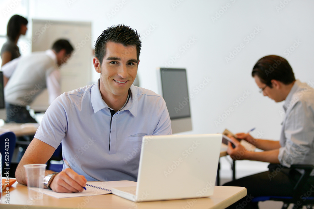 Jeune homme souriant en formation devant ordinateur Jeune homme souriant en formation devant ordinateur