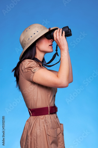 Obraz na plátně Woman in safari hat looking through binoculars side view