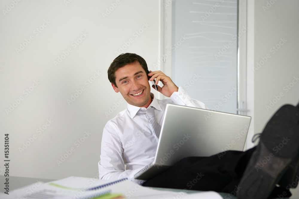 Homme assis à un bureau téléphonant devant un ordinateur Homme assis à un bureau téléphonant devant un ordinateur