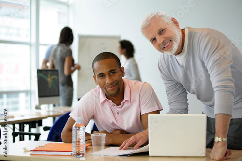 Hommes souriants au bureau avec documents devant un ordinateur