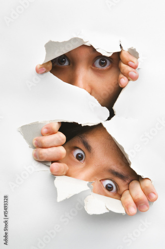 Two people peeking from hole in wall