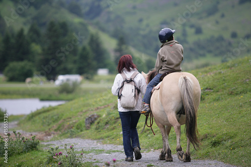 Femme marchant près d'un enfant assis sur un poney © auremar