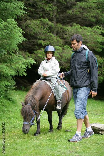 Homme marchant près d'un petit garçon assis sur un poney