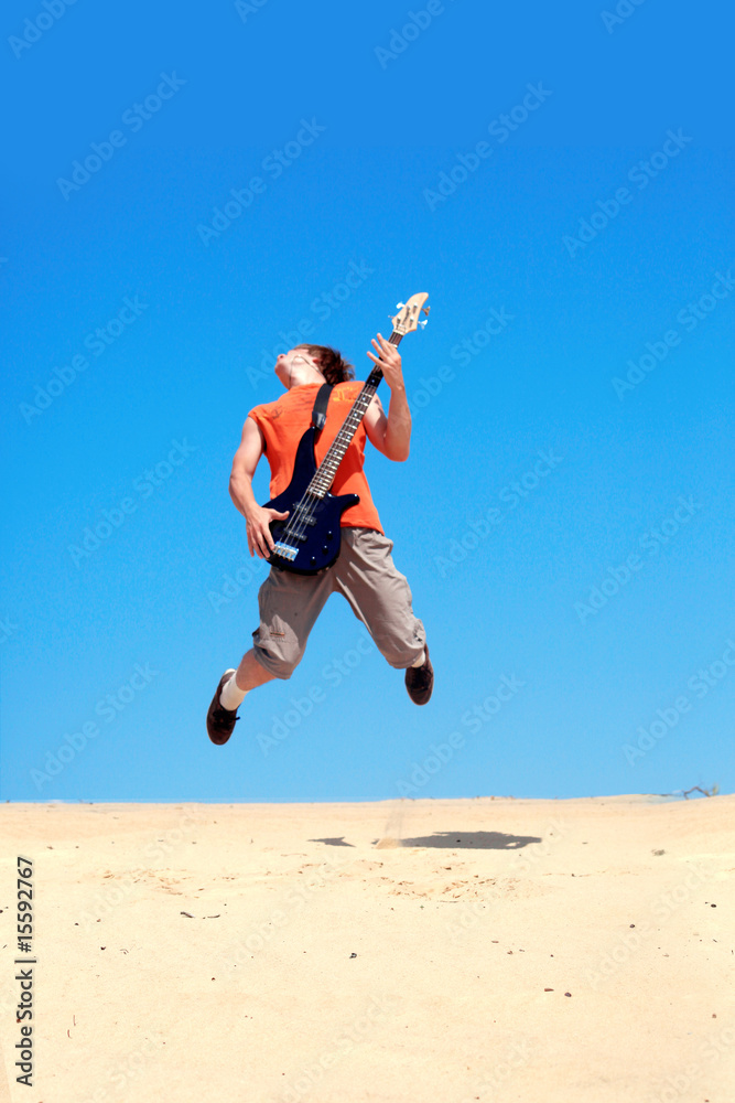Young man with guitar jumping on a background of blue sky Young man with guitar jumping on a background of blue sky