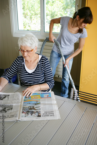 Femme sénior assise lisant le journal près d'une femme de ménage photo