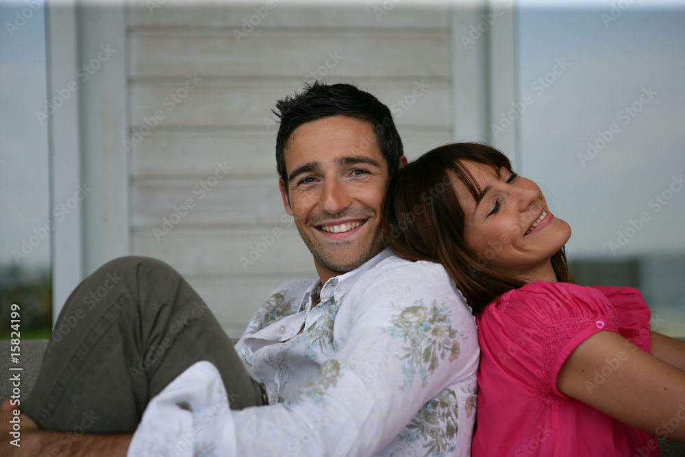 Jeune couple souriant assis sur un canapé dos à dos Jeune couple souriant assis sur un canapé dos à dos