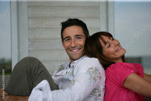 Jeune couple souriant assis sur un canapé dos à dos