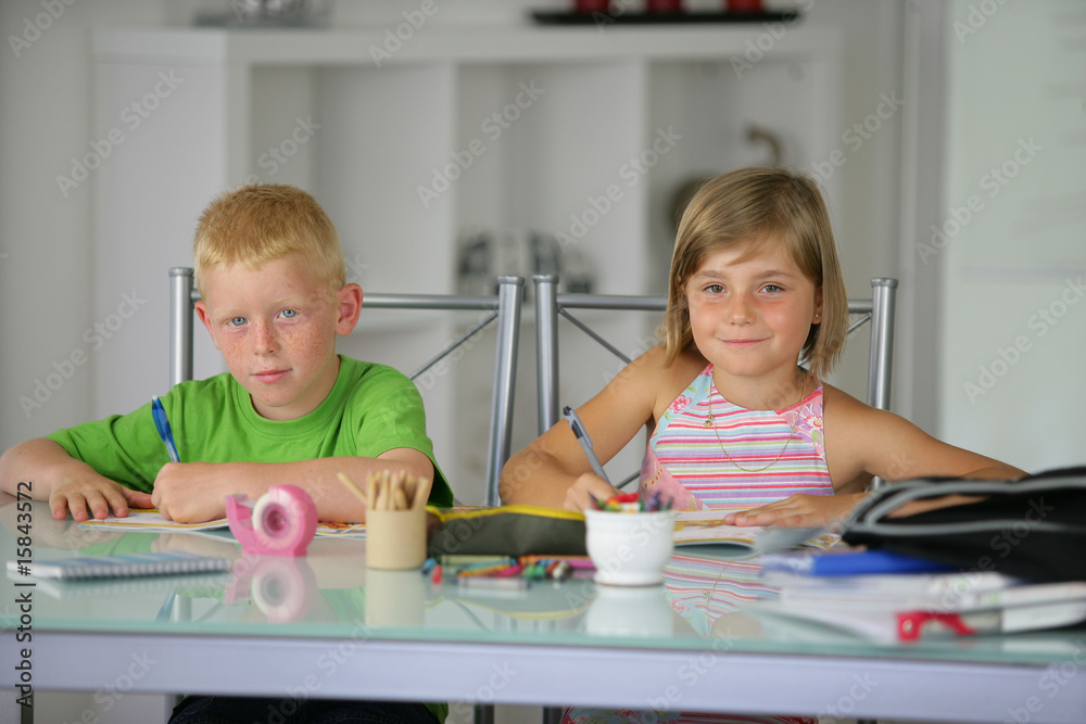 deux enfants souriants assis à un bureau faisant leurs devoirs