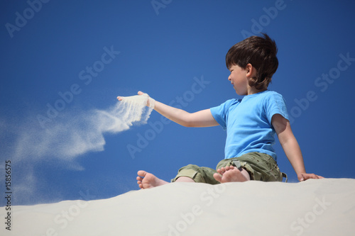 Canvas Print boy sits on sand and scatters it