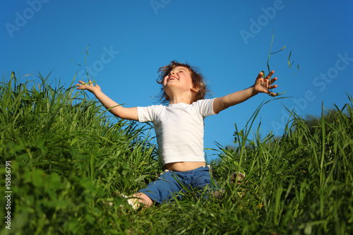 little girl sits in grass and looks upwards
