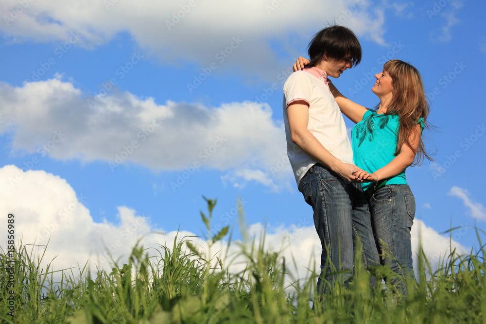 young pair holds each other in grass against sky young pair holds each other in grass against sky