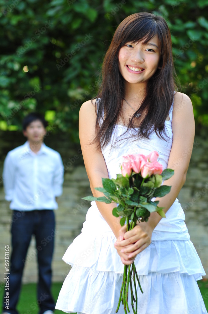 Asian Woman Holding A Bouquet Of Roses With Man Standing Behind Asian Woman Holding A Bouquet Of Roses With Man Standing Behind