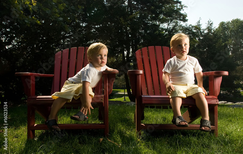 Twin Baby Brothers Sitting on red Lounge Chairs enjoying summer