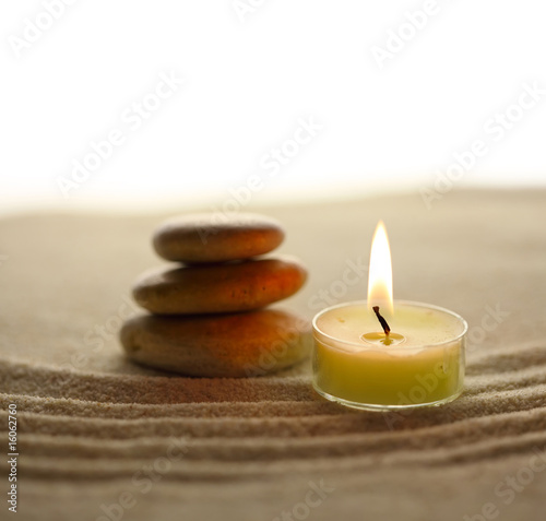 Stack of pebbles and light candle on sand