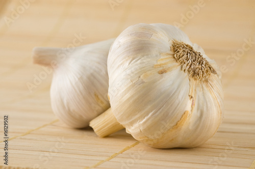 Two garlic heads on a bamboo mat.